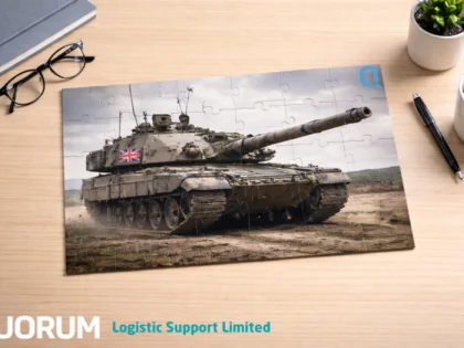 Completed jigsaw puzzle of a British Army tank on a minimalist wooden desk with glasses, notebook, pen, coffee cup and plant.